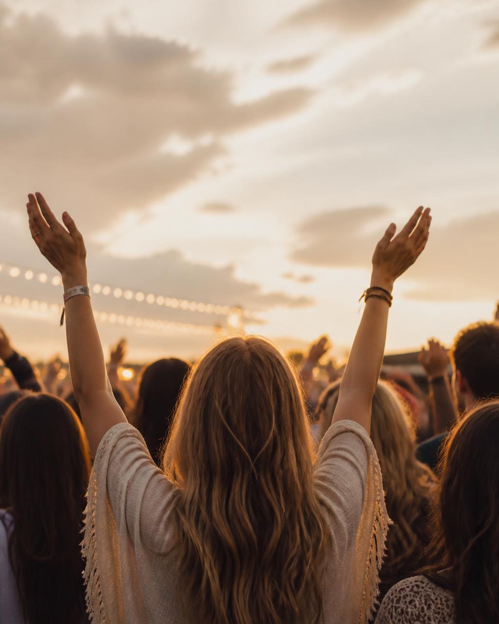 Festival-goers at sunset with hands in the air